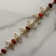 a gold bracelet with red glass beads and filigrees on the clasp is sitting on a marble surface