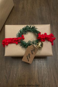 a present wrapped in brown paper with red pom - poms and a christmas wreath