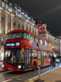 a red double decker bus driving down a street next to tall buildings and traffic lights