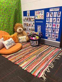 a teddy bear sitting on an orange chair in front of a bulletin board and colorful rug