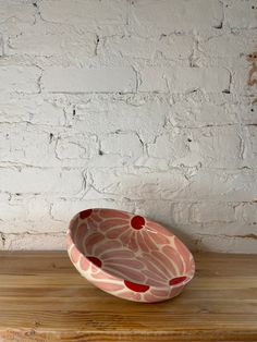 a red and white bowl sitting on top of a wooden table next to a brick wall