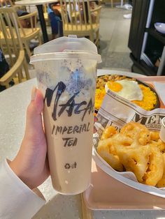 a person holding up a cup with some food in front of them on a table