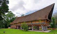 an old building with a thatched roof in the middle of a grassy area surrounded by trees