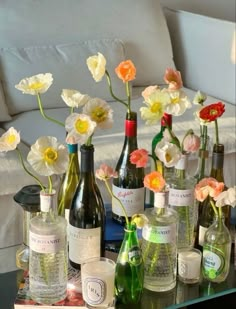 a table topped with bottles and flowers on top of a glass table next to a couch