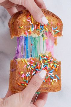 a person holding a piece of bread with sprinkles and rainbow colored icing