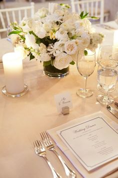 the table is set with white flowers and silverware