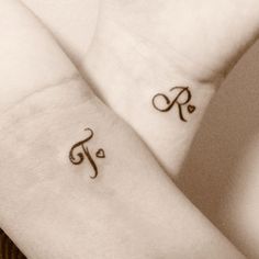 two small tattoos on the arms of someone's arm and wrist, both with initials