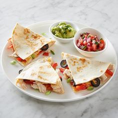 three quesadillas on a white plate with salsa and guacamole