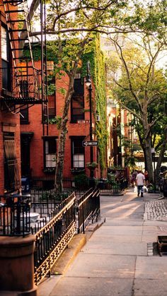 a man walking down a street next to tall buildings with trees on each side and stairs leading up to the second story