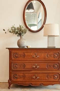 a wooden dresser with a mirror above it and a lamp on the table next to it