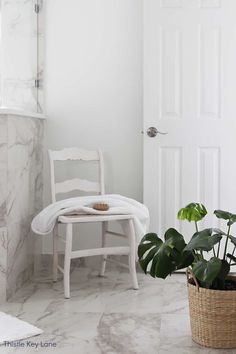 a white chair sitting next to a potted plant on top of a table in a bathroom