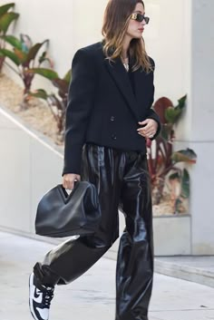 a woman in black jacket and leather pants walking down the street with her handbag