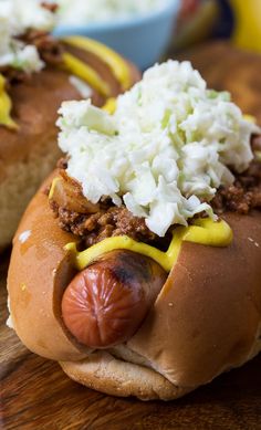 two hot dogs with mustard, onions and cheese on them sitting on a cutting board