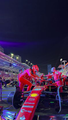 some people in red racing cars on a race track at night with lights and spectators