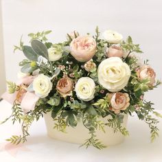 a bouquet of white and pink flowers in a vase with greenery on the side