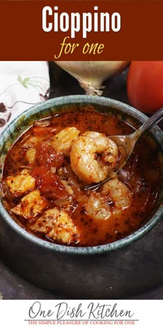 a bowl filled with shrimp and tomato soup on top of a table next to an apple