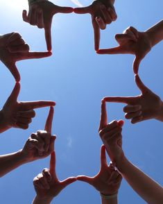 many hands are holding together in the shape of a star against a blue sky background