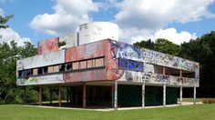 an old building with graffiti on it in the middle of a field and trees behind it