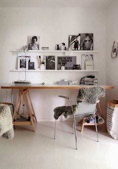 a desk with two chairs and pictures on the wall above it in a white room