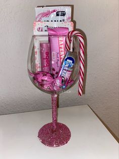 a wine glass filled with pink items and candy cane on top of a white table