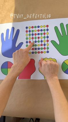 two hands are pointing at an array of handprints on a piece of paper