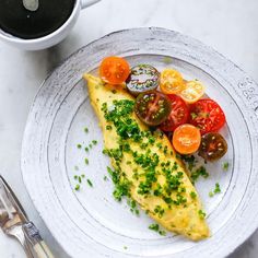 an omelet with tomatoes and chives on a plate next to a cup of coffee