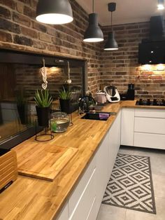 a kitchen with white cabinets and wooden counter tops next to a brick wall that has hanging lights above it