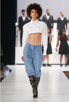 a model walks down the runway wearing high waisted jeans and white shirt with black tuxedos