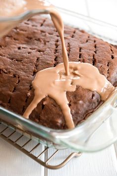 someone pouring chocolate sauce on top of a brownie in a glass baking dish with a wire rack