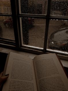 an open book sitting on top of a window sill next to a rainy street