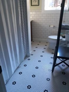 a white toilet sitting next to a shower in a bathroom under a window with curtains