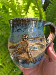 a hand holding a blue and brown cup with a dragonfly on it