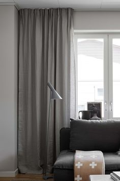 a living room filled with furniture and a large window covered in grey drapes