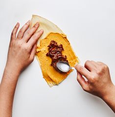 two hands are spreading peanut butter on top of the tortilla shell with a spoon