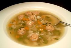 a bowl of soup with meatballs and carrots in it on a white plate