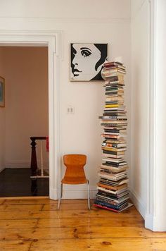 a stack of books sitting on top of a hard wood floor next to a chair