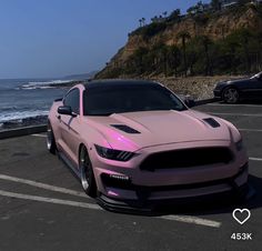 a pink mustang parked in a parking lot next to the ocean