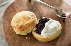 a wooden plate topped with two biscuits covered in butter and jelly next to a spoon