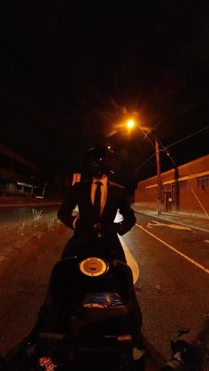 a man riding on the back of a motorcycle down a street at night with his hands on his hips