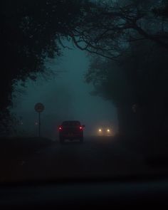 two cars driving in the dark on a foggy road with trees and street signs