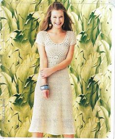 a woman standing in front of a wall with green leaves on it and wearing a white crocheted dress