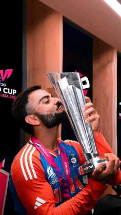 a man holding a silver trophy in his hand and looking up at the sky while wearing an orange shirt