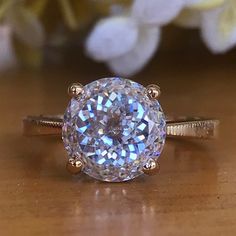 a close up of a ring on a wooden surface with flowers in the background,