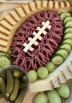 a football shaped cheese board with grapes, cucumbers and pickles