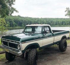 a green and white truck parked next to a lake