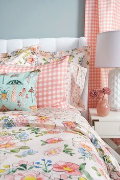 a bed with pink gingham sheets and white headboard next to a lamp