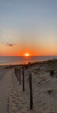 the sun is setting over the beach with fenced in sand and water behind it