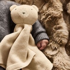 a teddy bear wrapped in a blanket is held by someone's hand on a pile of fur