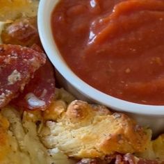 a white plate topped with bread and pizza next to a bowl of tomato sauce on top of it