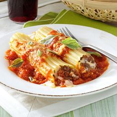 a white plate topped with ravioli and meat covered in sauce next to a glass of red wine